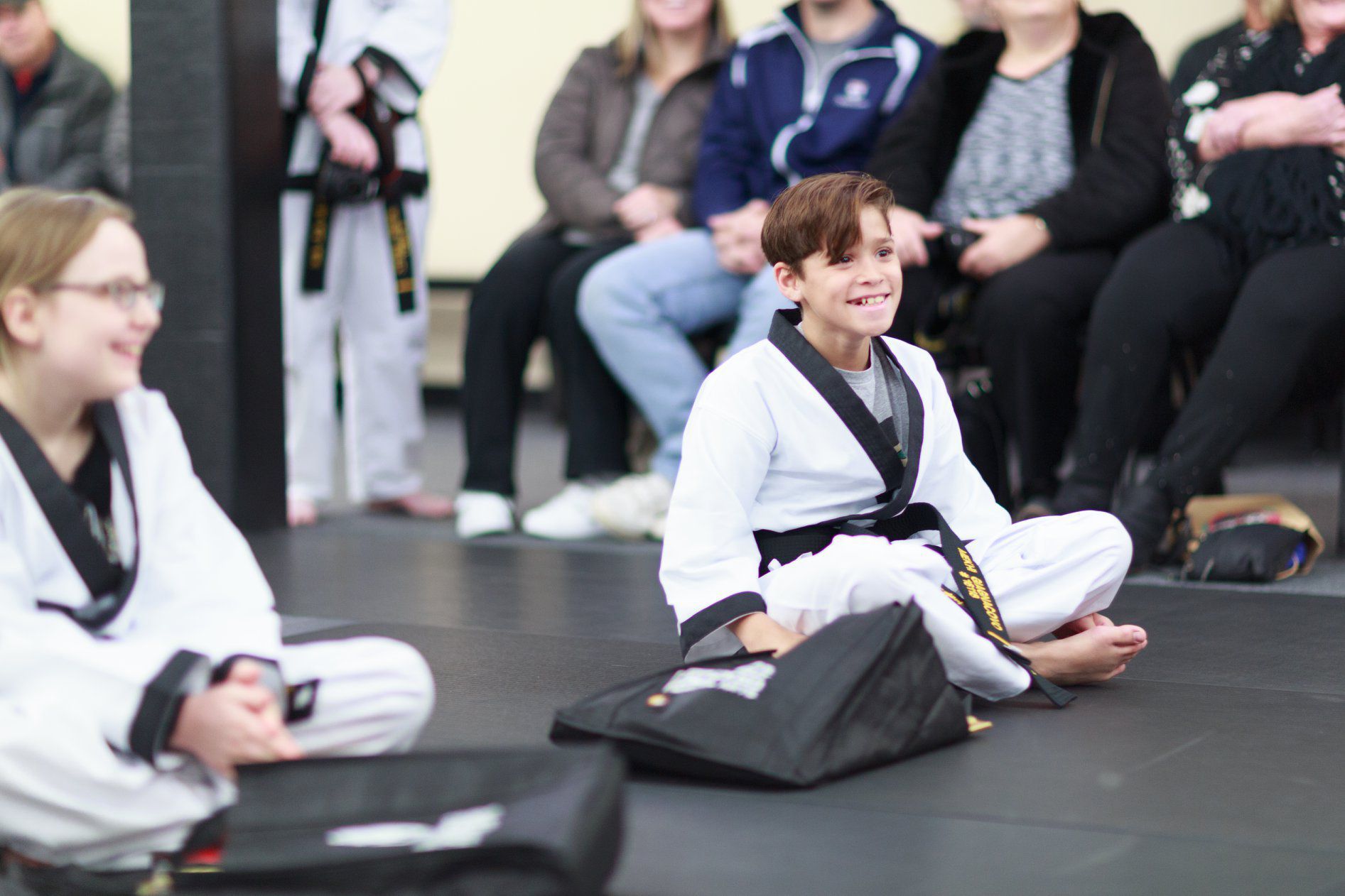 a boy in a white karate uniform sits on the floor