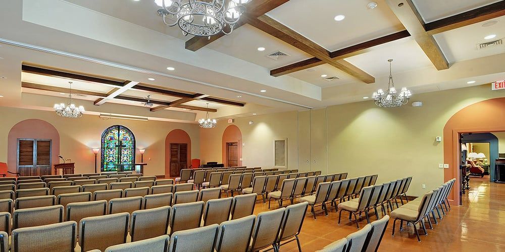 Empty chapel with rows of chairs, stained-glass windows, and chandeliers on a vaulted ceiling