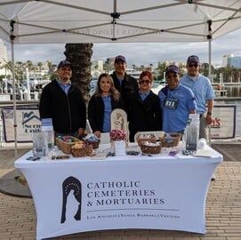 People behind a tent table for Catholic Cemeteries & Mortuaries at an outdoor event with flyers and bowls
