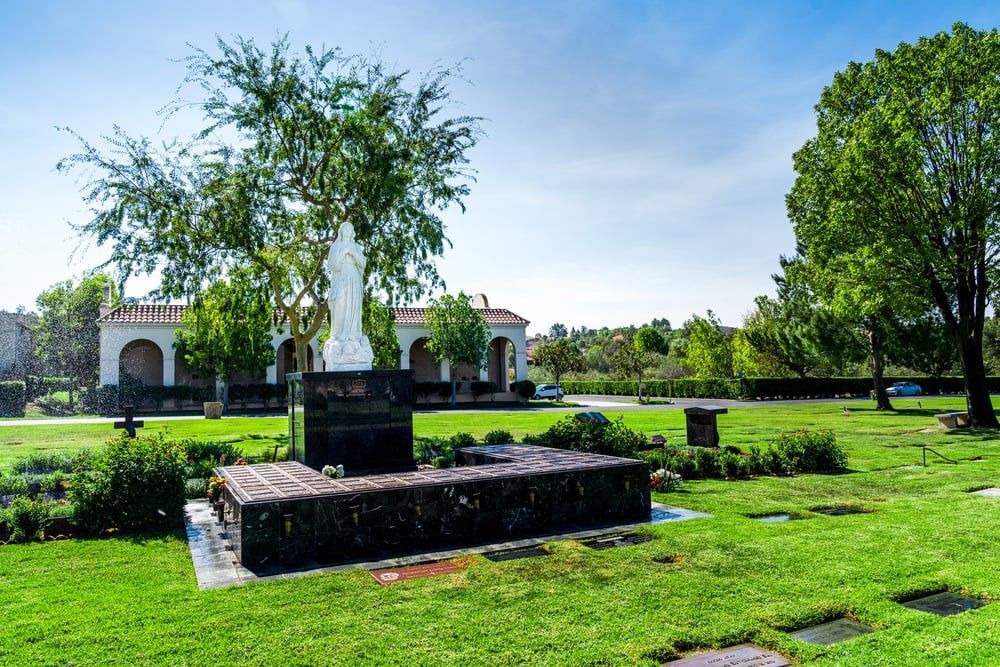 Green park with a white statue on a black pedestal, trimmed hedges, and a building in the background.
