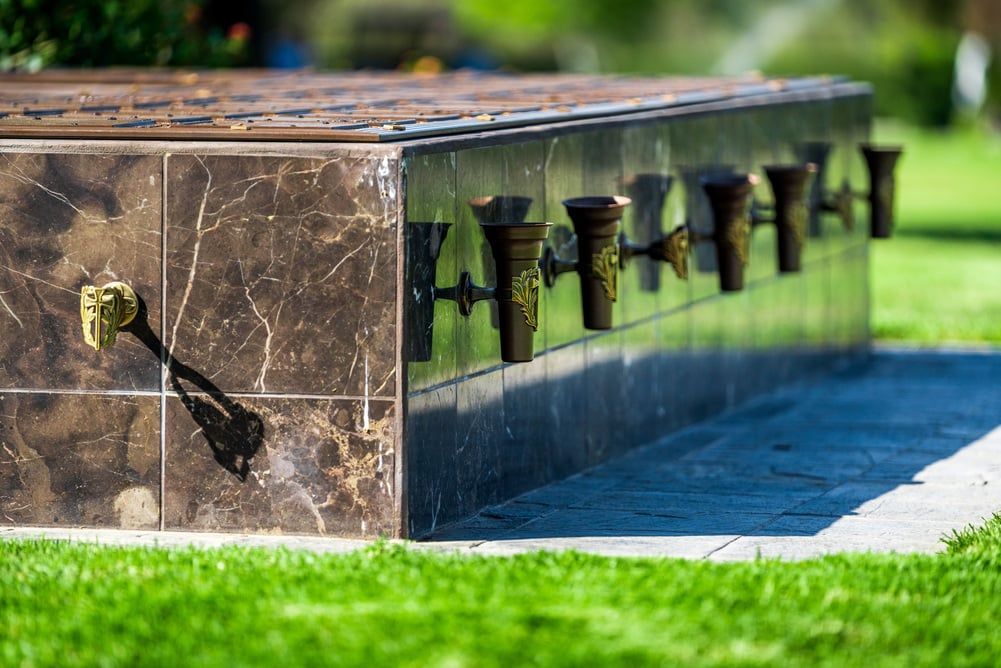 Stone memorial wall with engraved plaques and a handrail in a green park