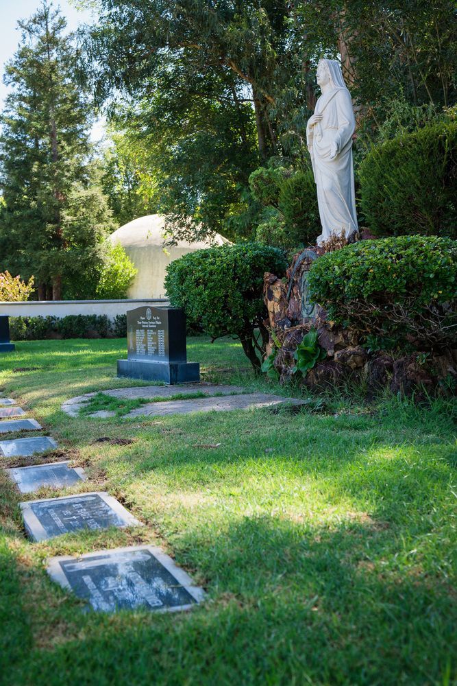 Gravestones and a white statue in a sunny cemetery with green grass and trees
