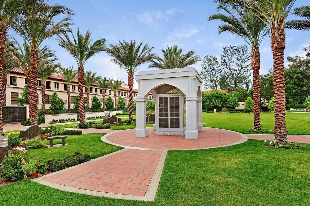 Palm-lined courtyard with a small white pavilion and brick path in a manicured garden
