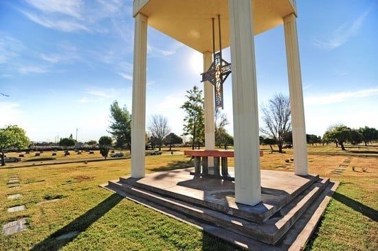 White gazebo or monument with a bronze statue in a sunny park on a grassy field.
