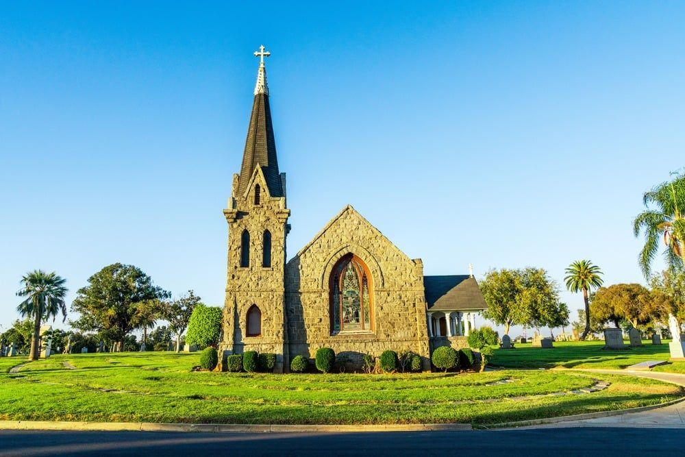Stone church with tall steeple on a green lawn under a clear blue sky.