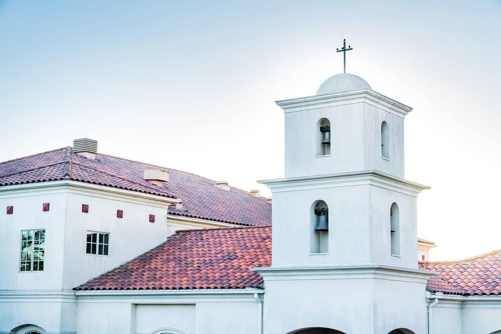 White church with red-tiled roofs and a small bell tower topped by a cross under a clear sky