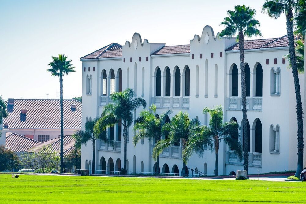 White Spanish-style building with palm trees and a green lawn under a clear blue sky