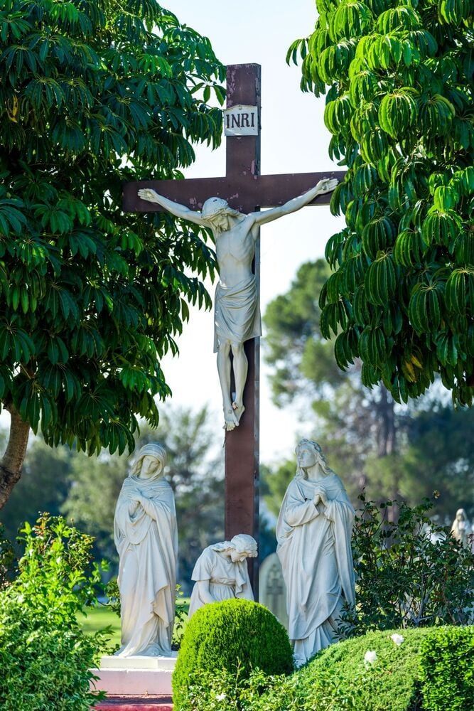 Crucifix with Jesus in a green garden, flanked by statues and trees