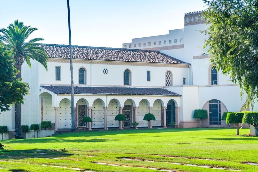 White colonial-style building with arched walkway and green lawn under blue sky