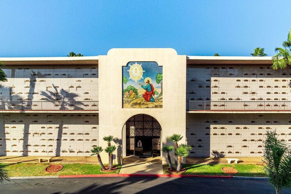 Front view of a white stucco building with a colorful mural above the arched entrance.