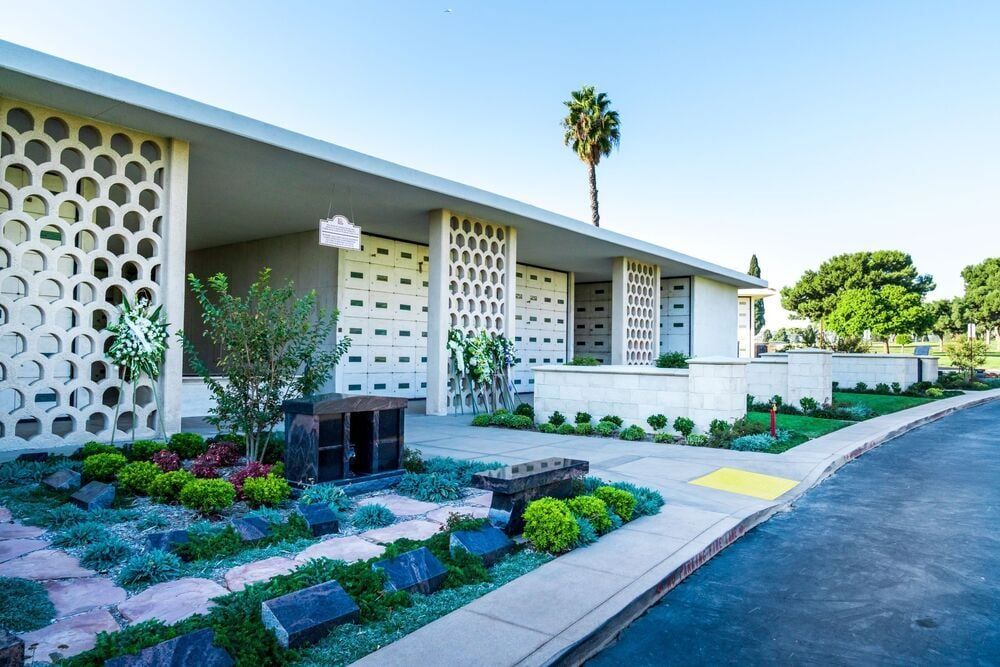 Modern building exterior with white lattice walls, landscaped garden beds, and a driveway under clear blue sky