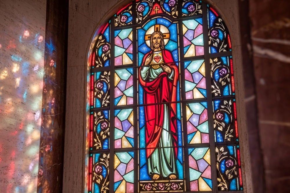 Stained glass window showing a robed religious figure with a halo in red, blue, and gold