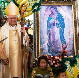 Pope in ceremonial robes beside framed Our Lady of Guadalupe image, with children and flowers at a parade