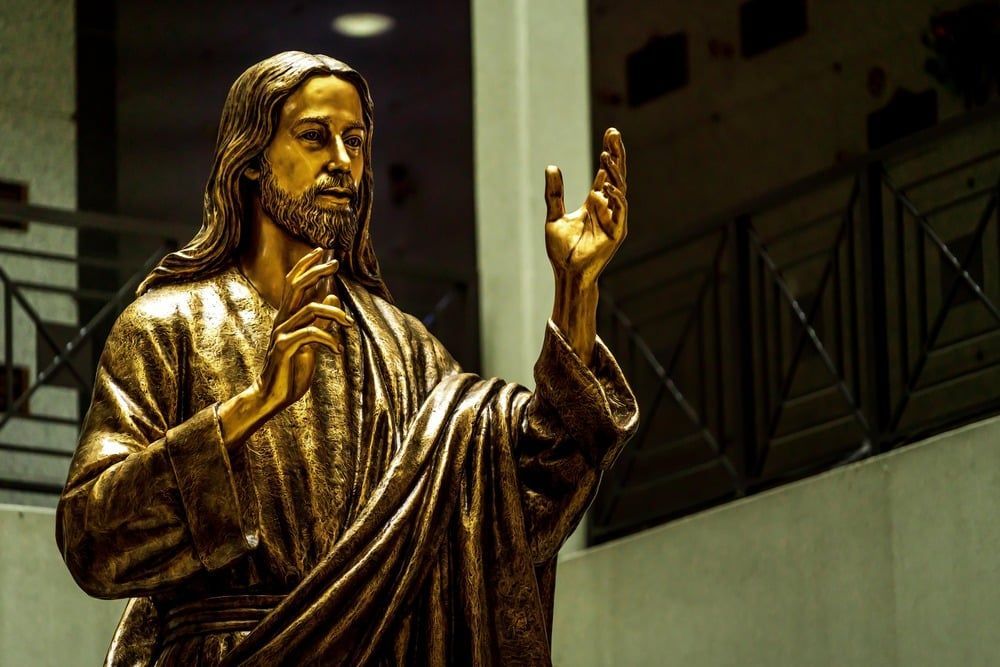 Golden statue of a robed figure with raised hand and clasped heart in a dim indoor setting