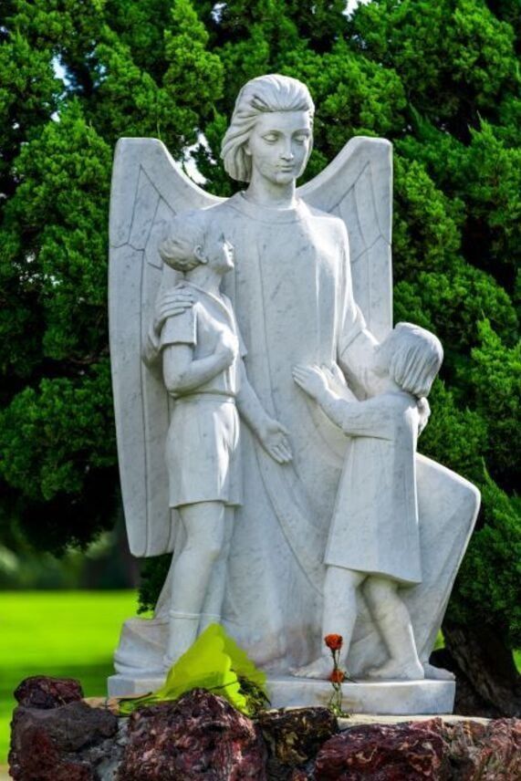 White angel statue with wings holding children in a green garden