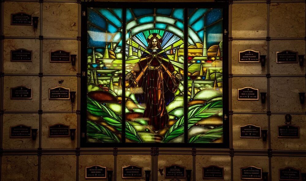 Stained-glass panel of a robed figure with outstretched arms, set in a wall of mailboxes.