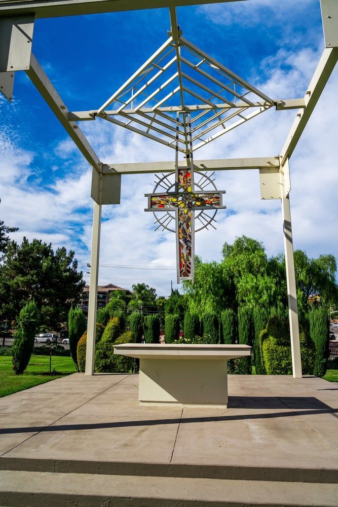 Outdoor altar with a crucifix under a white canopy, surrounded by trees and steps.