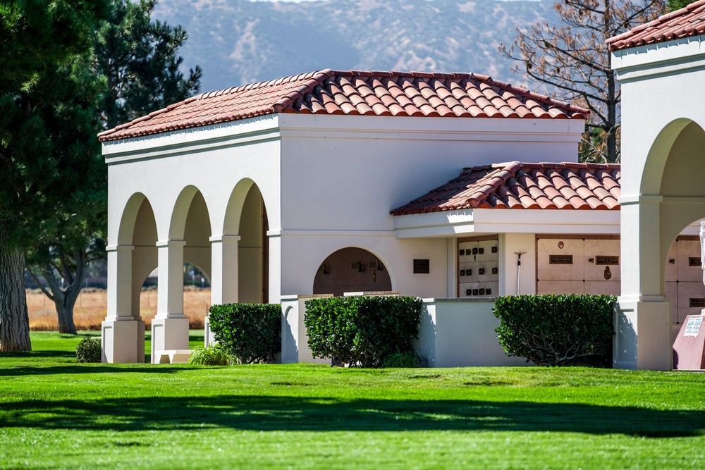 Spanish-style building with white arches, red-tile roof, and trimmed hedges beside a green lawn