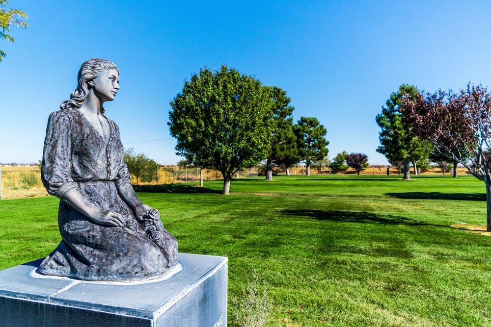 Bronze seated statue on a pedestal in a sunny green park with trees and blue sky