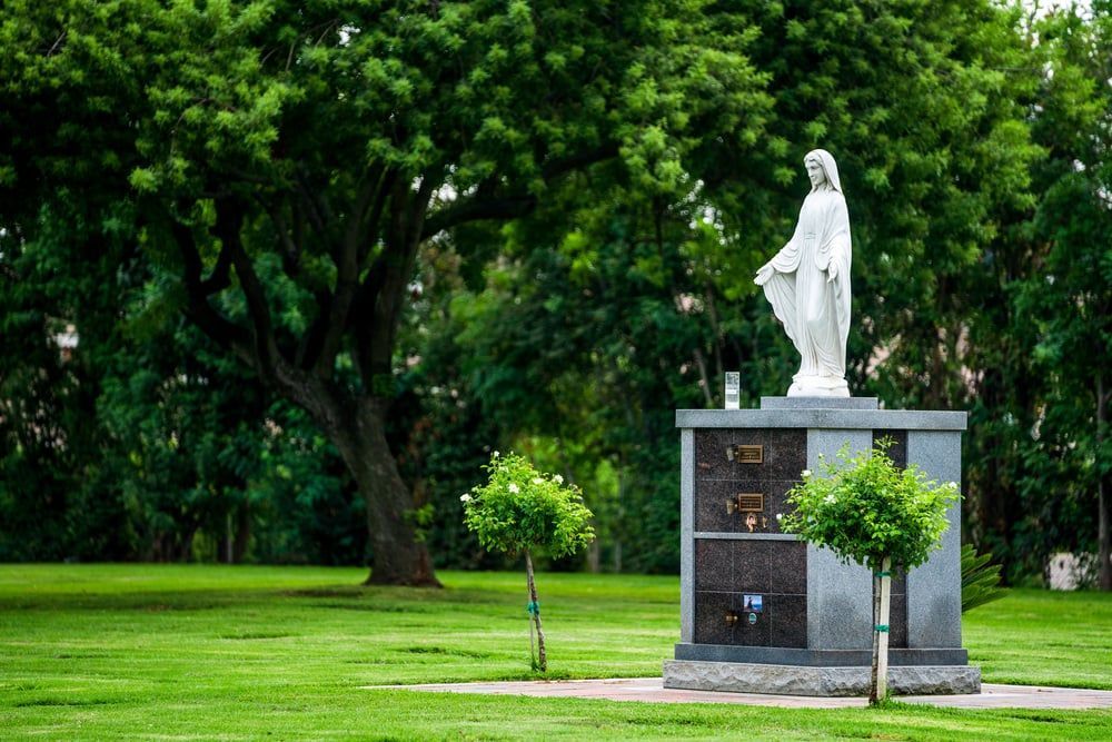 White statue on a stone pedestal in a green park surrounded by trees and grass