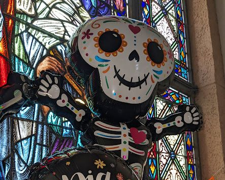 Day of the Dead skeleton figure with colorful painted skull and black outfit before stained glass window