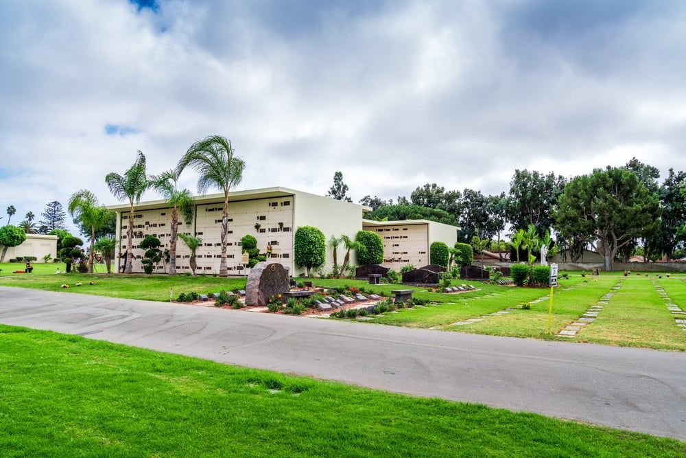 Modern beige building with palm trees, green lawn, and driveway under a cloudy sky