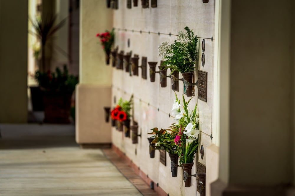 Wall of hanging flower pots along a covered walkway, with red and green plants