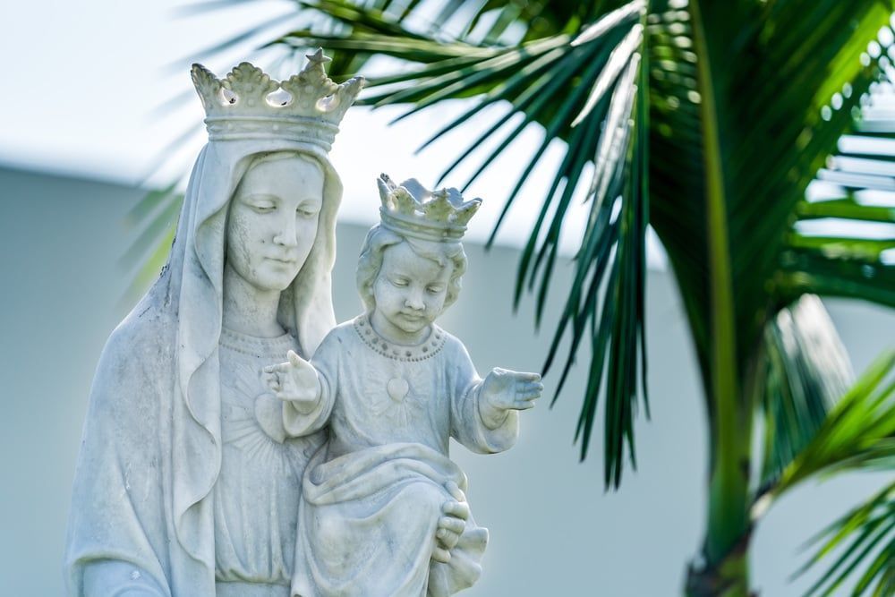 White statue of the Virgin Mary and child with palm leaves in the background