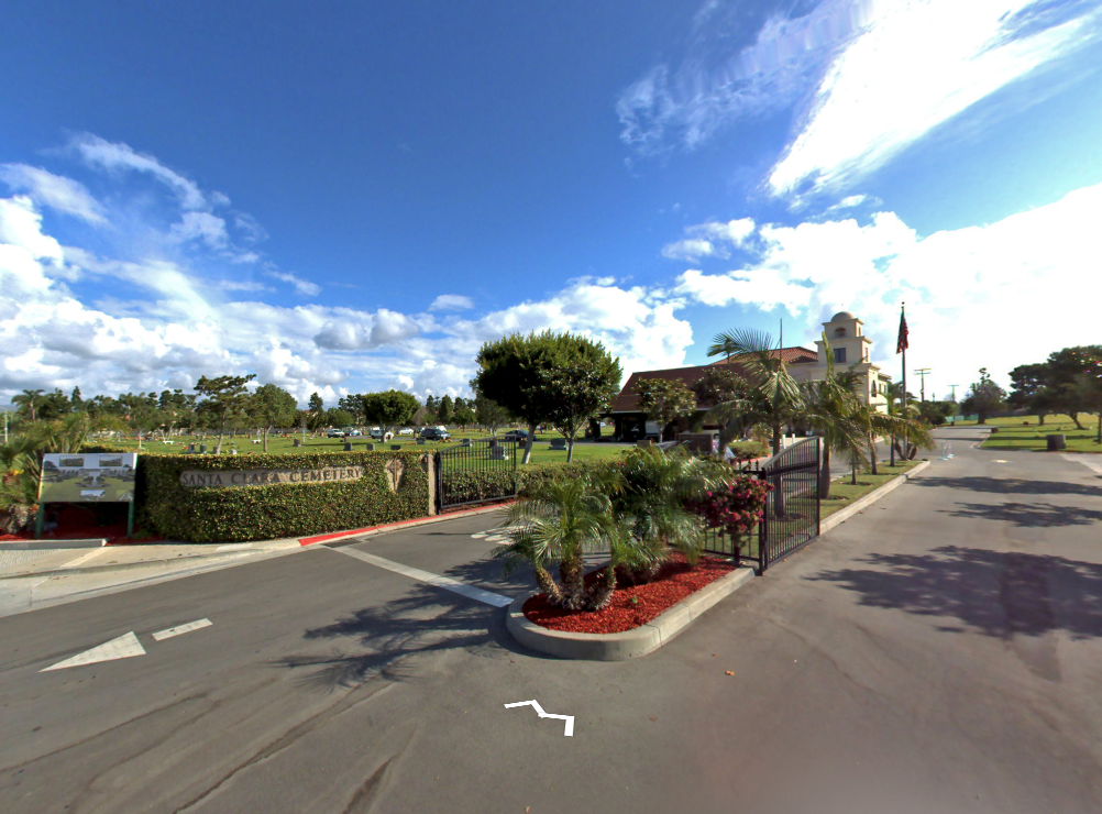 Road intersection with landscaped median, hedges, and a building under a bright blue sky