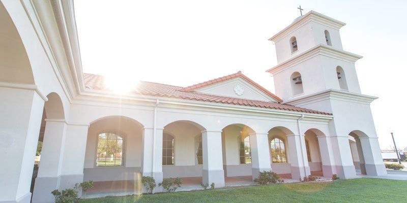 White stucco church with arched colonnade and bell tower in bright sunlight