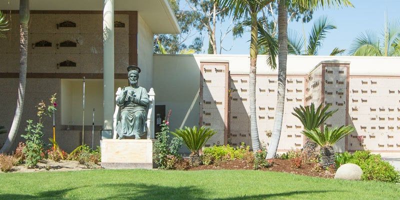 Bronze statue in a landscaped courtyard with palm trees and a modern building backdrop