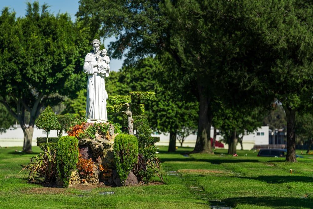 White statue on a flower-covered pedestal in a green park with trees and grass