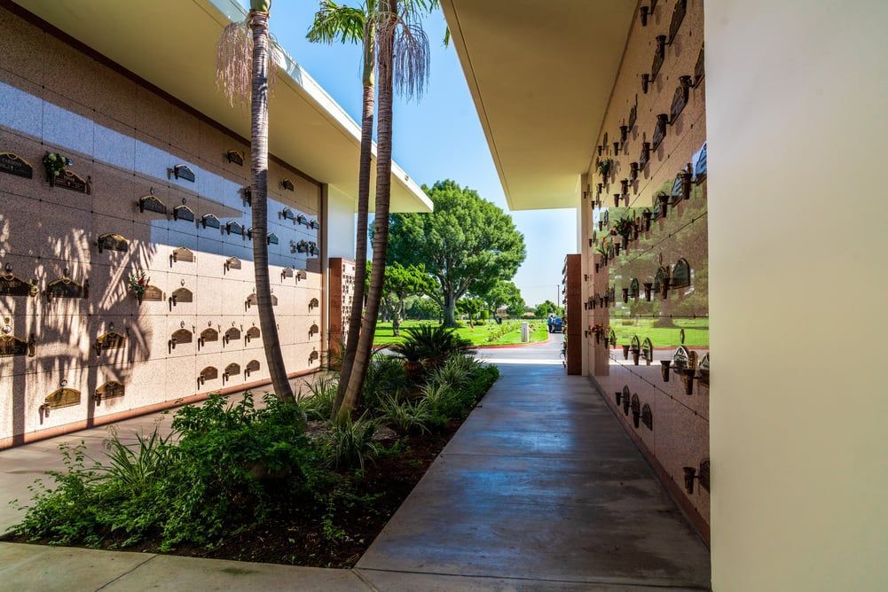 Outdoor walkway between beige buildings with greenery and sunlight at the end