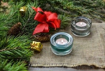 Christmas greenery with red ribbon, gift boxes, and lit candles on burlap fabric