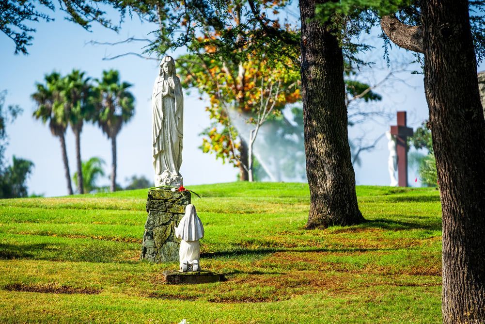 Statue in a sunny park with green grass, trees, and a red cross in the background