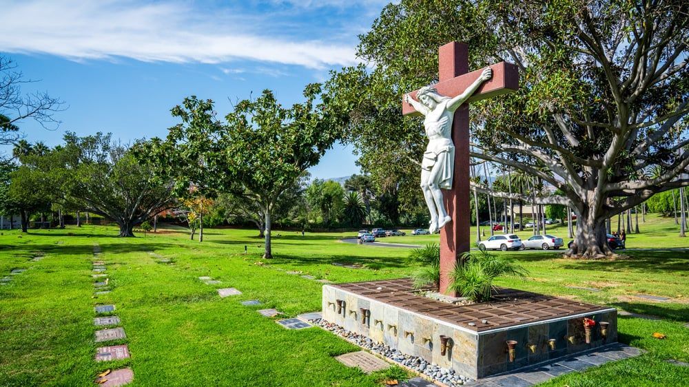 Crucifix in a green park under a blue sky, with trees and a paved path nearby