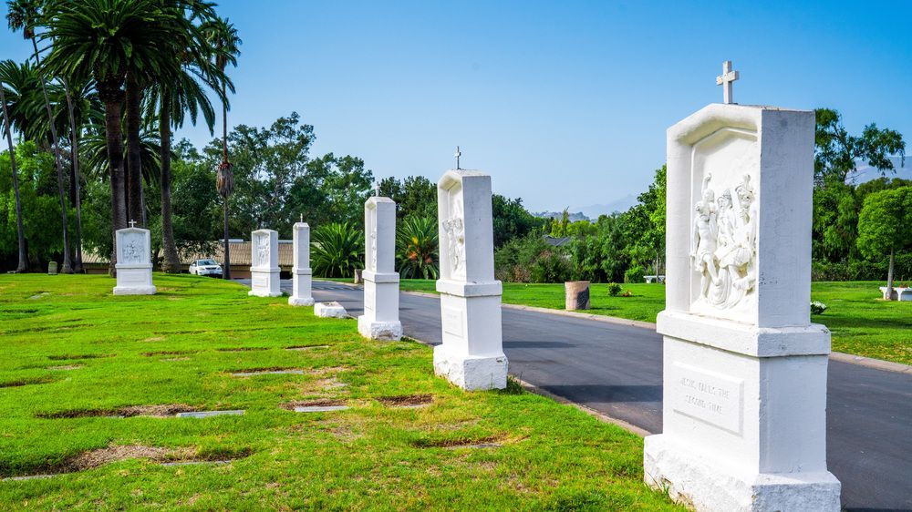 White memorial pillars lining a paved path through a green cemetery under a bright blue sky