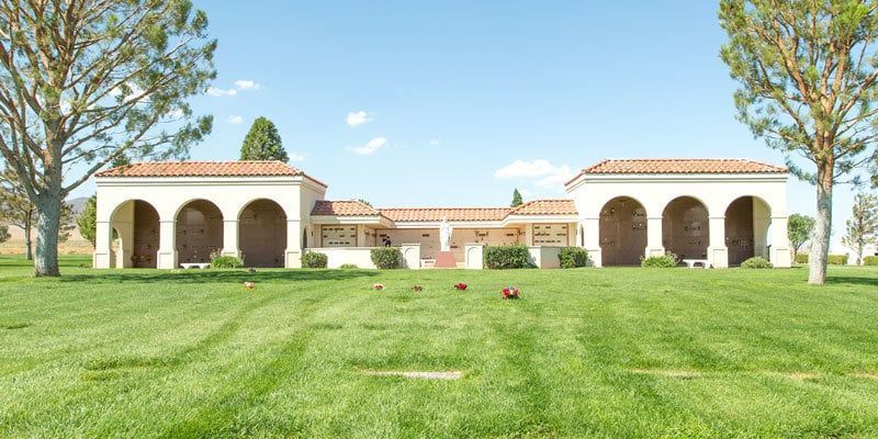 Sunny courtyard with green lawn and white arches framing a red-tiled building under blue sky
