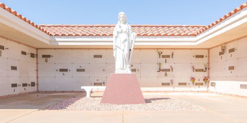 White statue on a pink pedestal in a tiled courtyard with red-tiled roof walls and blue sky