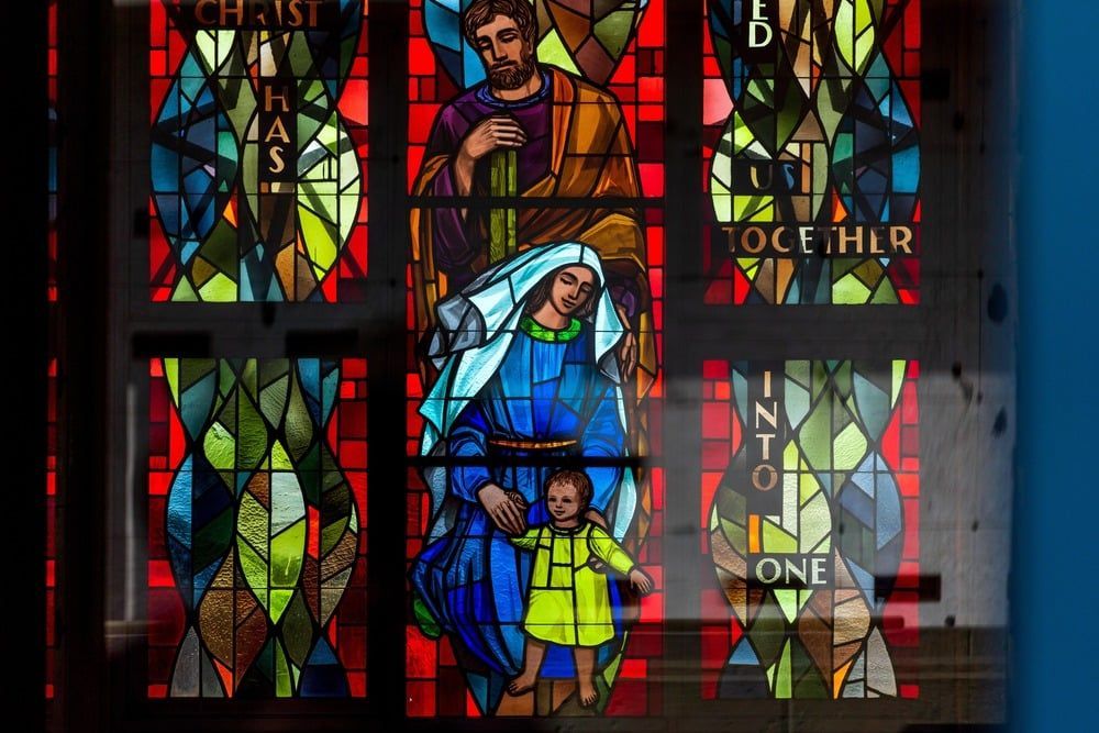 Stained-glass church window with colorful figures and the words “together” and “one.”
