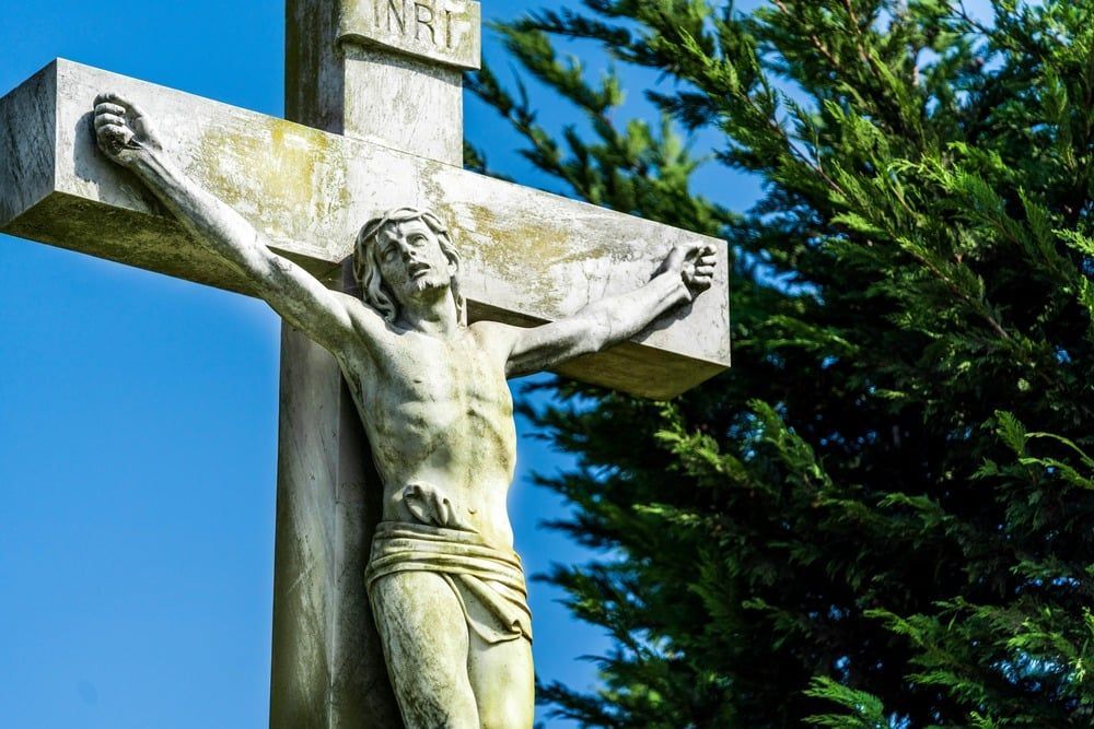 Stone crucifix of Jesus on a cross against blue sky and green trees