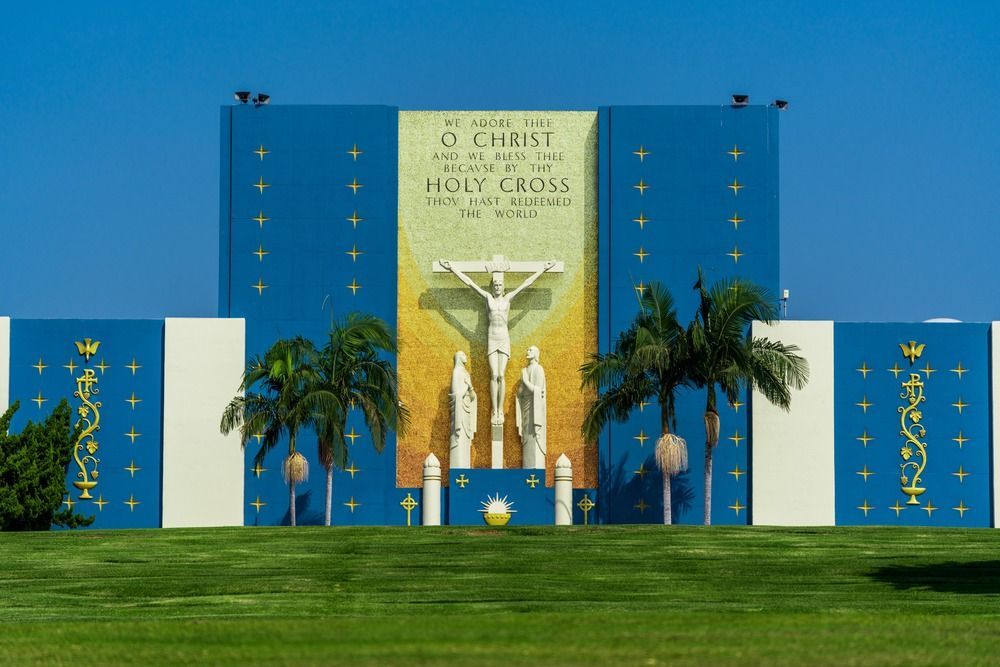 Blue church altar with a crucifix, gold banner, palm trees, and green lawn in front