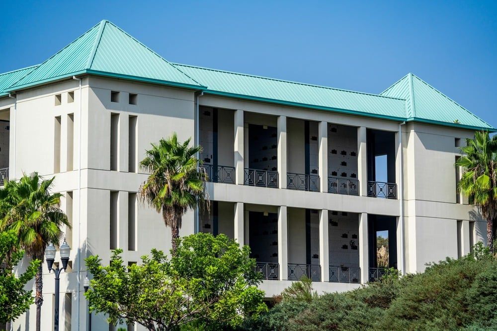 White building with teal roofs and palm trees against a blue sky