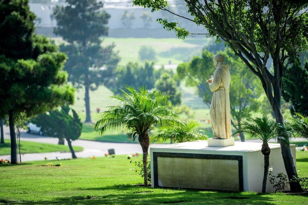 Statue on a pedestal in a green park with trees and a winding path