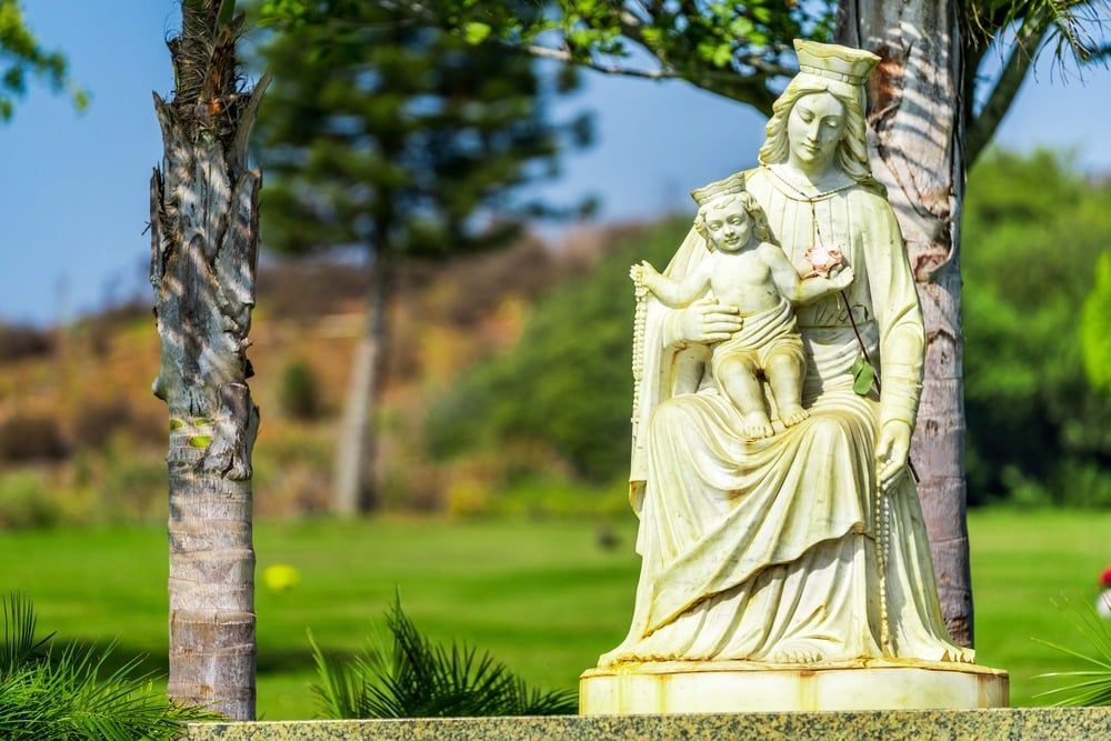 White stone statue in a green garden with palm trees and blurred lawn background
