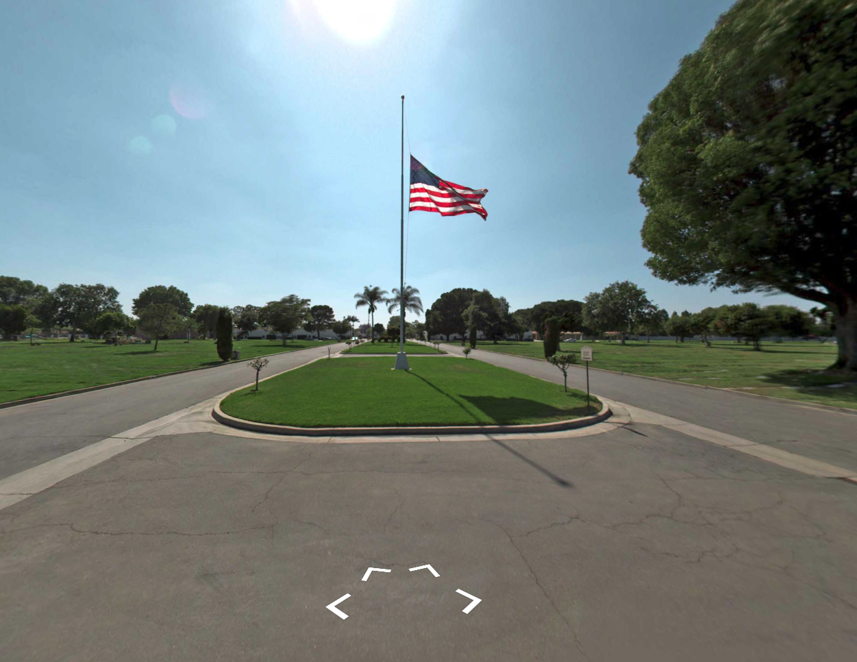 American flag flying over a landscaped park entrance under a bright blue sky