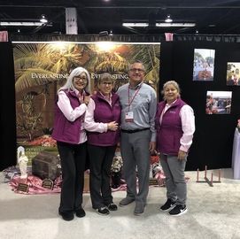 Four people in purple vests pose at a trade show booth with a forest-themed banner.