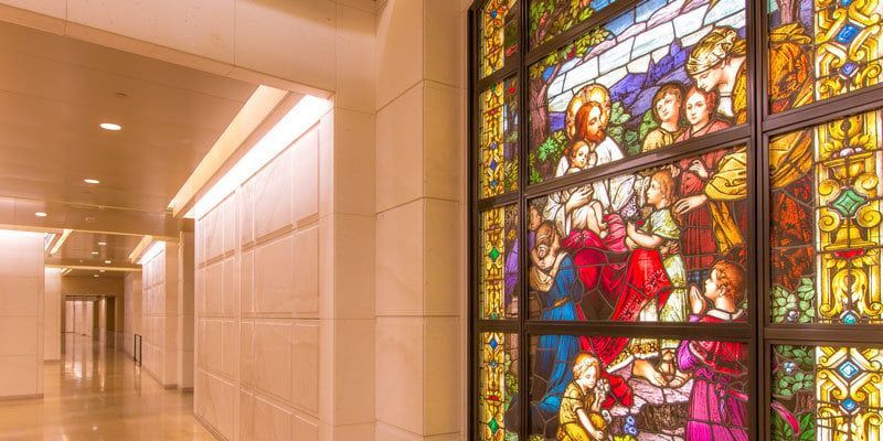 Bright hallway beside a colorful stained-glass window depicting biblical figures