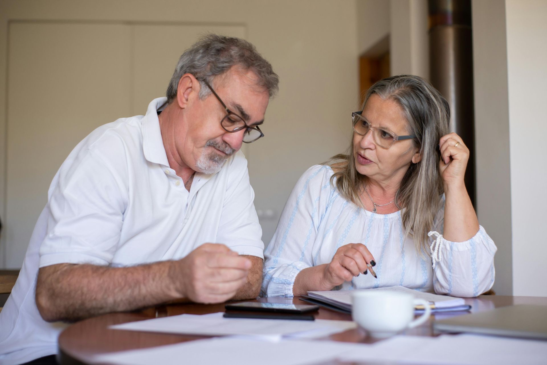 Two people reviewing documents at a table, with a tablet and a coffee cup nearby.