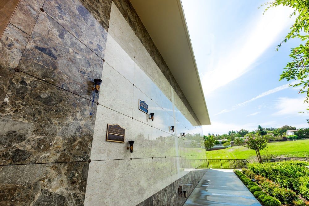 Modern stone wall with plaques beside a walkway and green garden under a bright sky